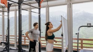 A gym coach instructs on whiteboard beside fitness equipment with mountain view.